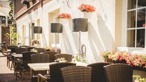 An outdoor café with wicker tables and chairs, potted plants, and hanging flower baskets. - Zum Vater Rhein (Monheim)