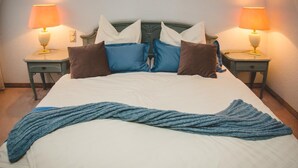 A neatly made bed with a blue knitted throw, two bedside tables with lamps, and a headboard with multiple pillows. - Zum Vater Rhein (Monheim)