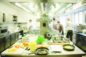 A commercial kitchen with stainless steel appliances, chefs preparing food, and various cooking utensils and ingredients on the counter. - Zum Vater Rhein (Monheim)