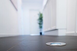 A modern, minimalist hallway with a circular object on the floor, possibly a sensor or device, and a blurred plant in the background. - Ca' Rebeka Venice (Mestre)