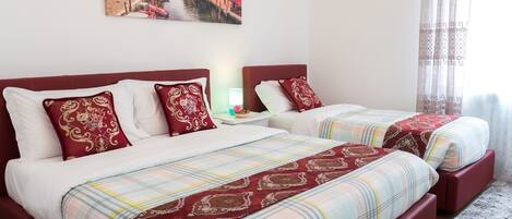 A hotel room with two beds, each with red and white bedding, a nightstand with a lamp, and a painting of a cityscape on the wall.