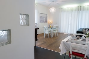 Un comedor con mesa de vidrio, sillas blancas y una araña.