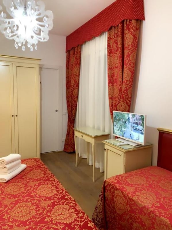 Habitación de hotel con dos camas, un escritorio con televisor, armario y candelabro.