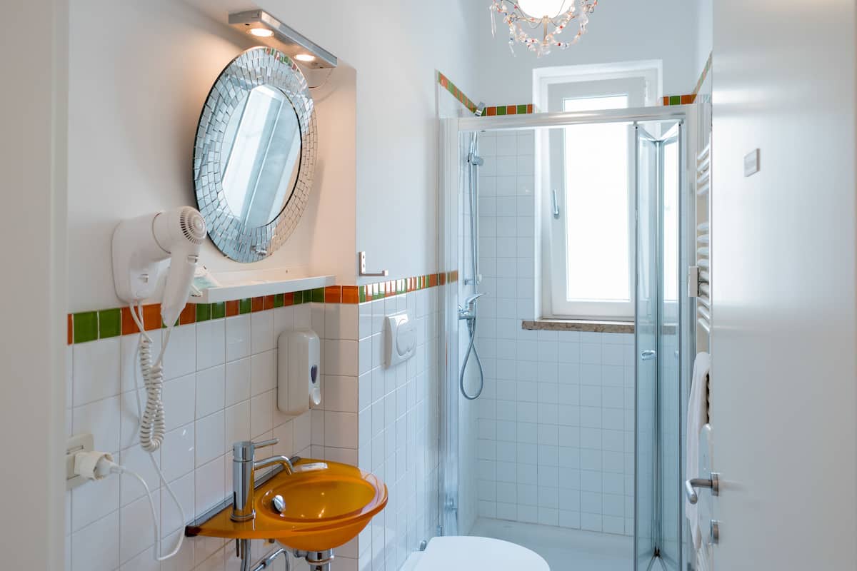 Ein Badezimmer mit einer Duschkabine, einem Waschbecken mit Spiegel darüber und einem an der Wand montierten Föhn.