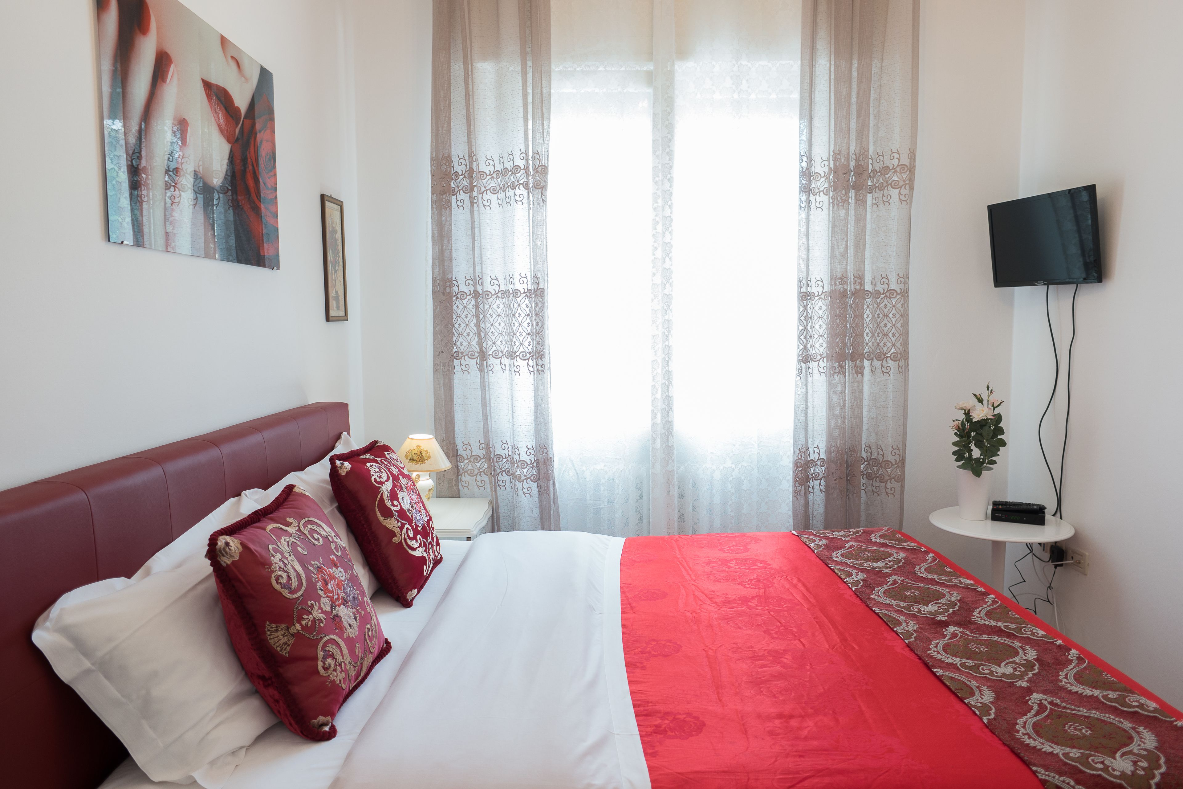 Een hotelkamer met een bed, een aan de muur bevestigde televisie en een raam met dunne gordijnen.