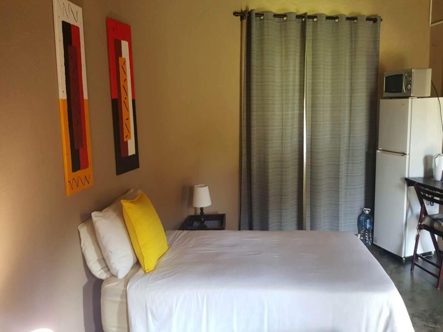 Una habitación de hotel con cama, escritorio, computadora, microondas y refrigerador.