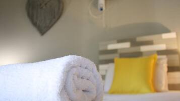 A neatly rolled white towel on a bed with a white and gray striped headboard, a yellow pillow, and a heart-shaped decoration on the wall.