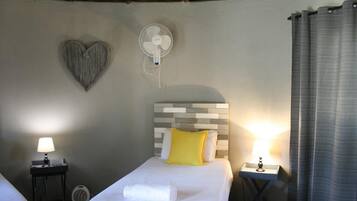 A hotel room with a bed, two bedside tables, a wall-mounted fan, a heart-shaped decoration, and a curtain.