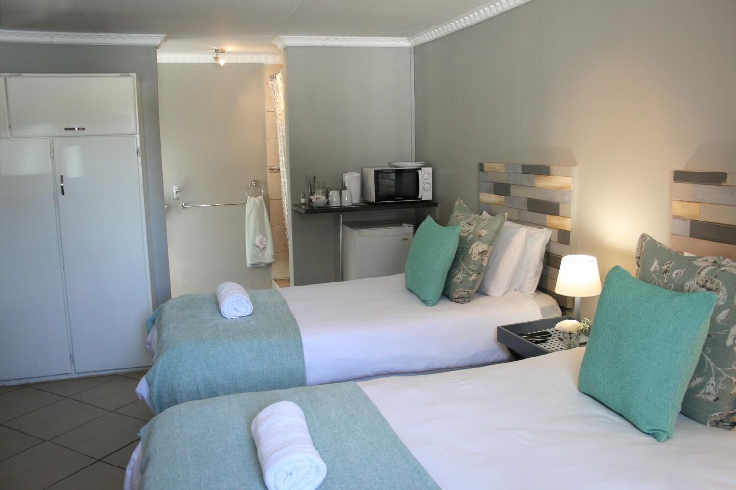 A hotel room with two beds, a TV, a microwave, and a small table with a lamp.