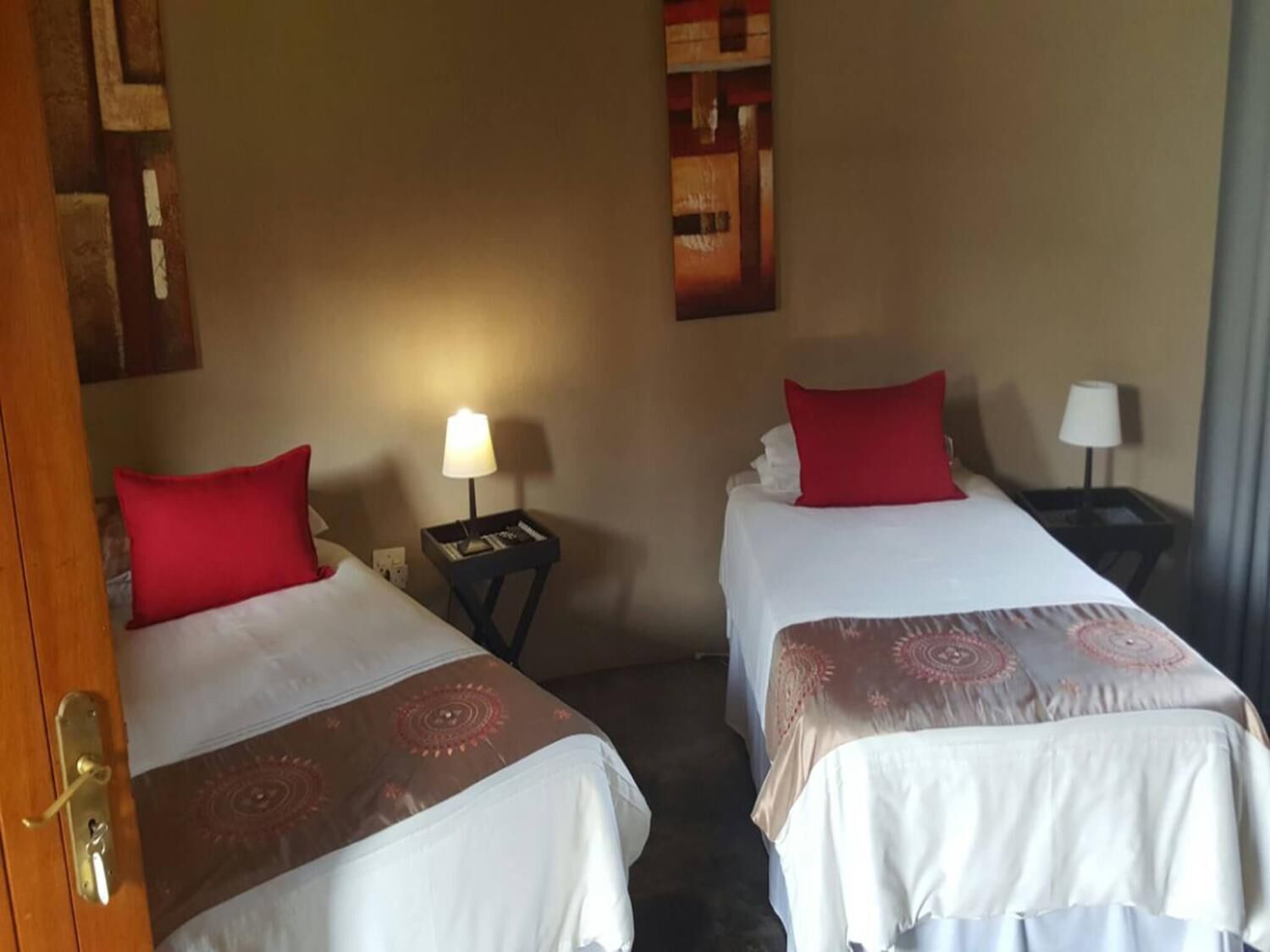 Two single beds with red pillows, a nightstand with a lamp, and a wall with a framed picture.