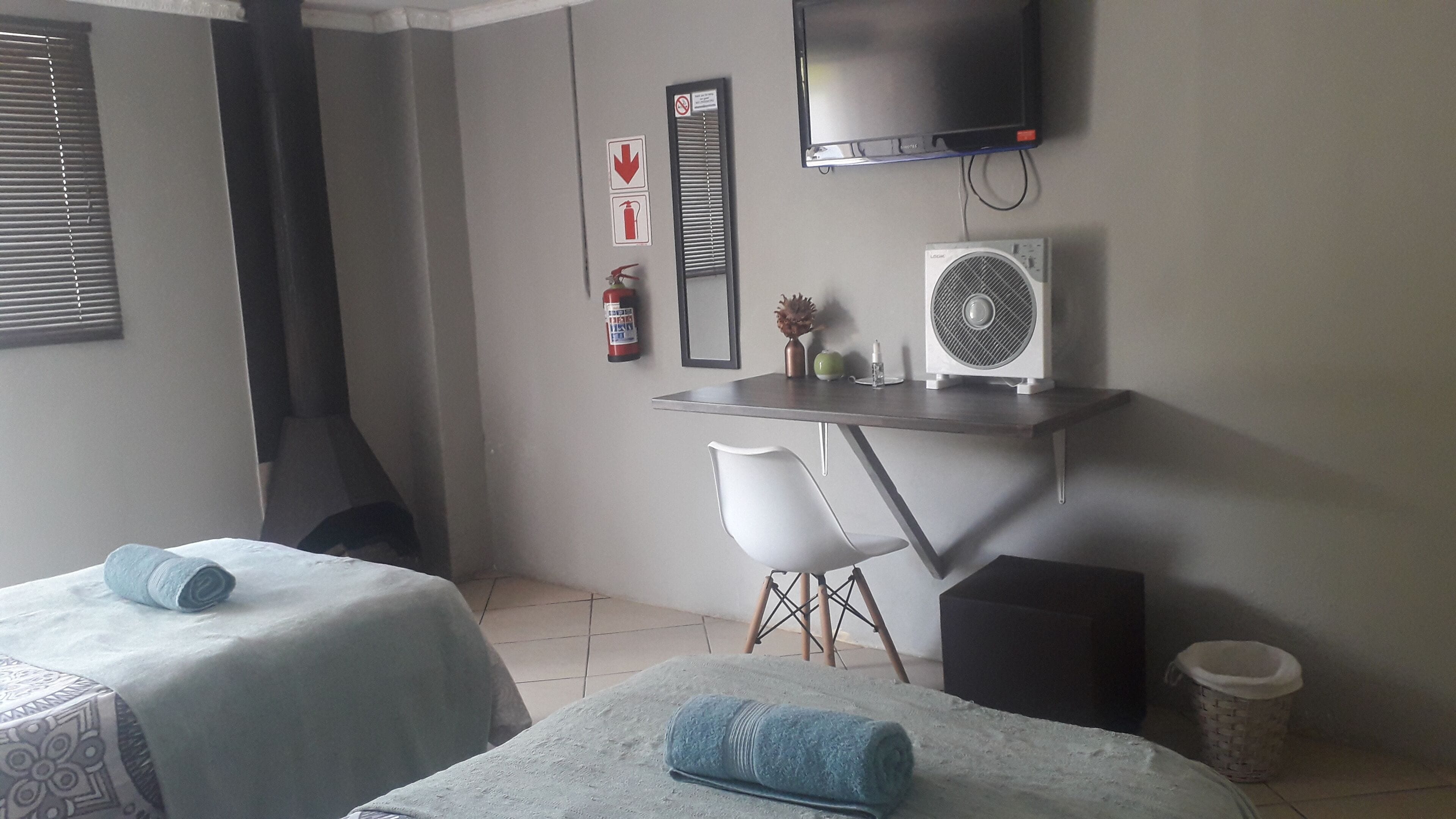 Ein Hotelzimmer mit zwei Betten, einem Schreibtisch mit Stuhl, einem Fernseher, einem Feuerlöscher und einer Heizung.