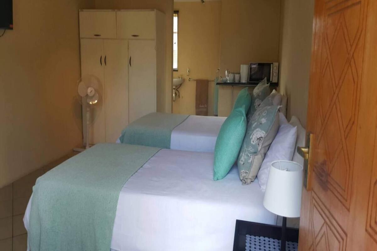 A bedroom with two beds, a wardrobe, a mirror, a sink, and a microwave.
