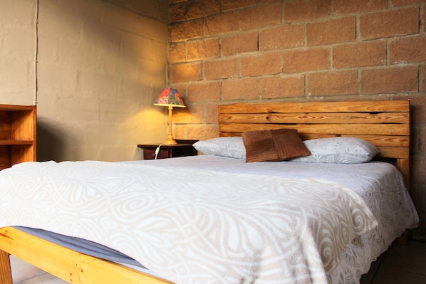 A single bed with a wooden headboard, a white patterned bedspread, and a brown pillow.