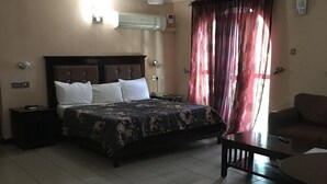 A hotel room with a bed, bedside tables, a sofa, and a window with curtains. - GQ International Hotel (Abuja)