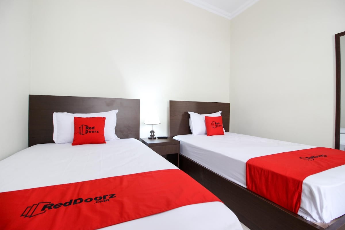 Two twin beds with white linens and red bedding, each with a pillow featuring the RedDoorz logo.