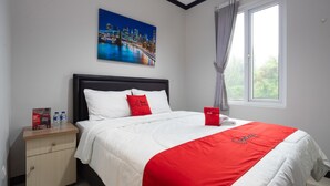 A hotel room with a bed, a nightstand, a window with curtains, and a cityscape painting on the wall. - Reddoorz Near Botani Square Mall (Bogor)