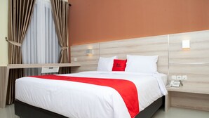 A neatly made bed with white and red bedding, a bedside telephone, and a wall-mounted light fixture.