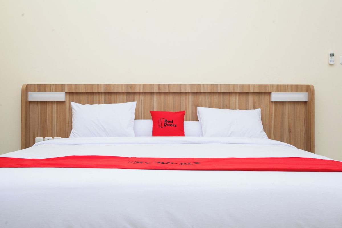 Un lit bien fait, avec une literie blanche et un oreiller rouge, une tête de lit en bois et un plaid rouge.
