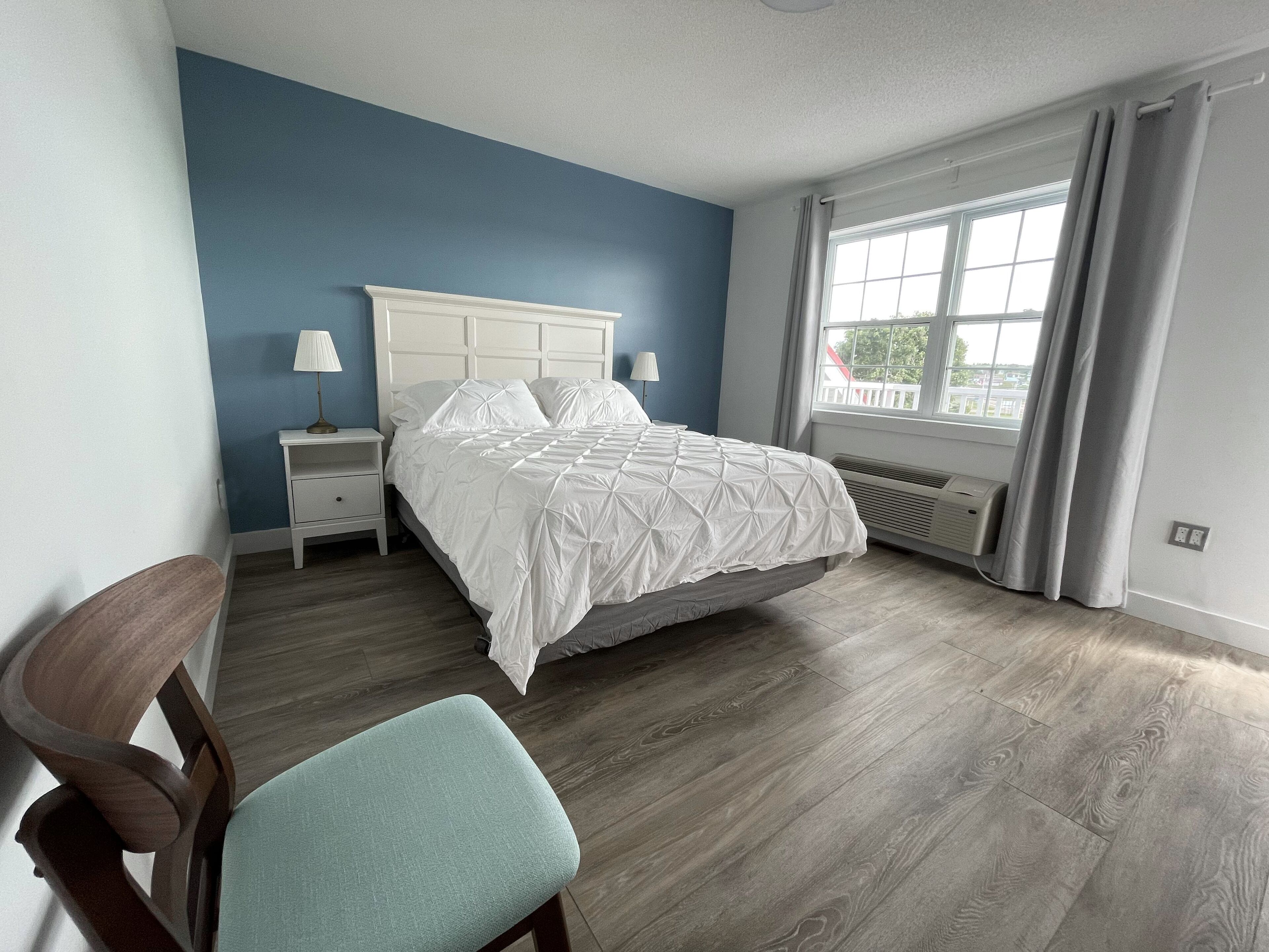 A bedroom with a bed, nightstands, a chair, a window with curtains, and a radiator.