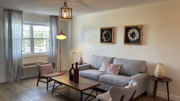 A living room with a grey sofa, two armchairs, a wooden coffee table, a floor lamp, and a small side table with a decorative item.