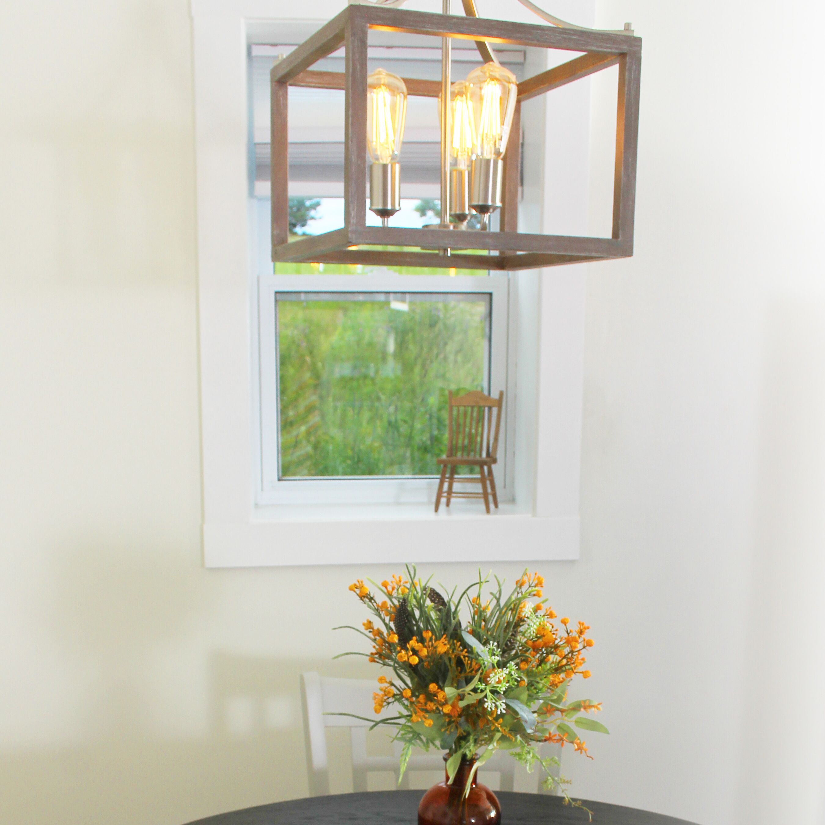 A dining table with a vase of flowers and a hanging light fixture above it.