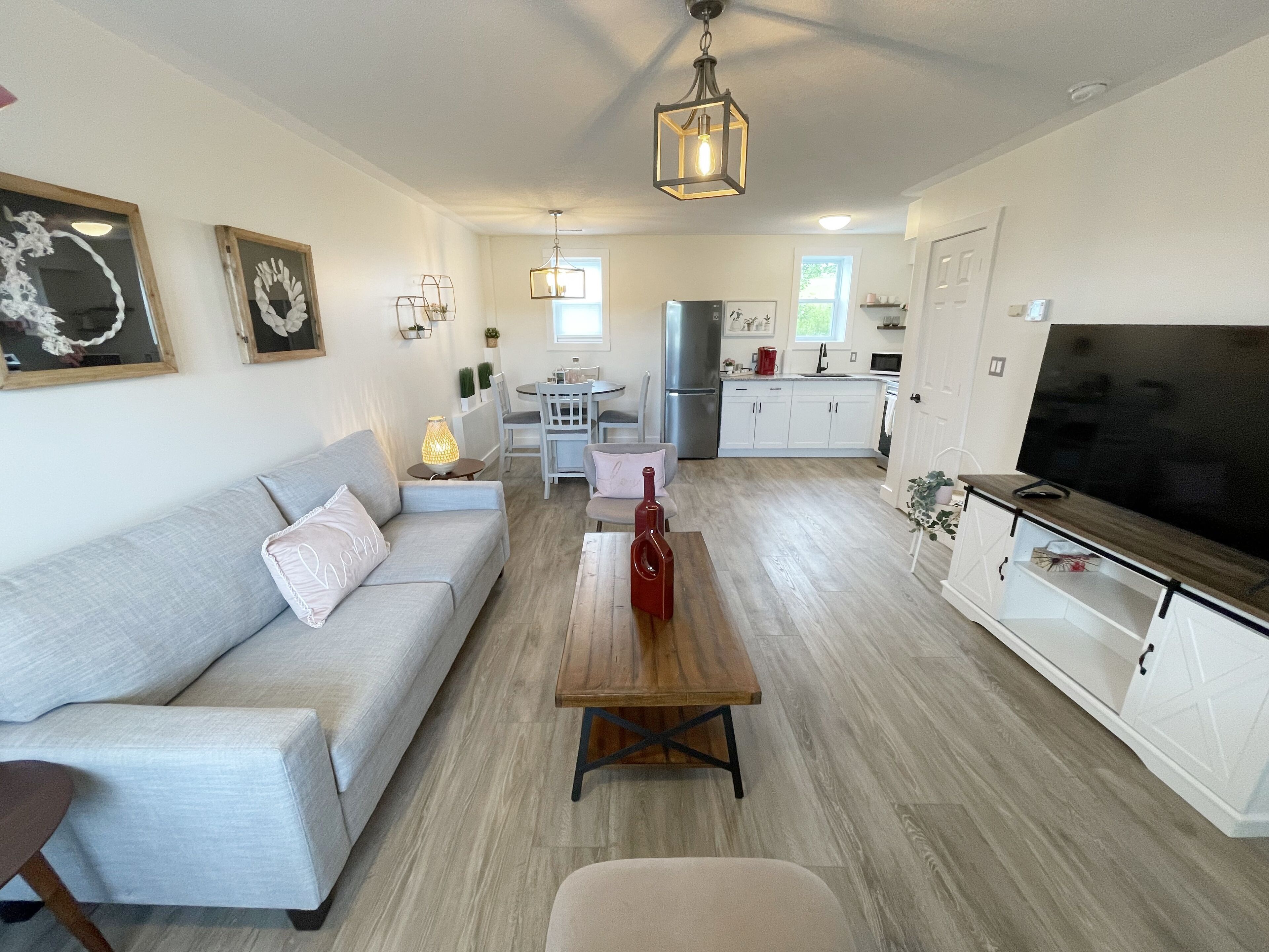 Una sala de estar moderna con un sofá, una mesa de centro y un mueble para televisión. Se observa un comedor con una mesa y sillas, y una cocina al fondo.