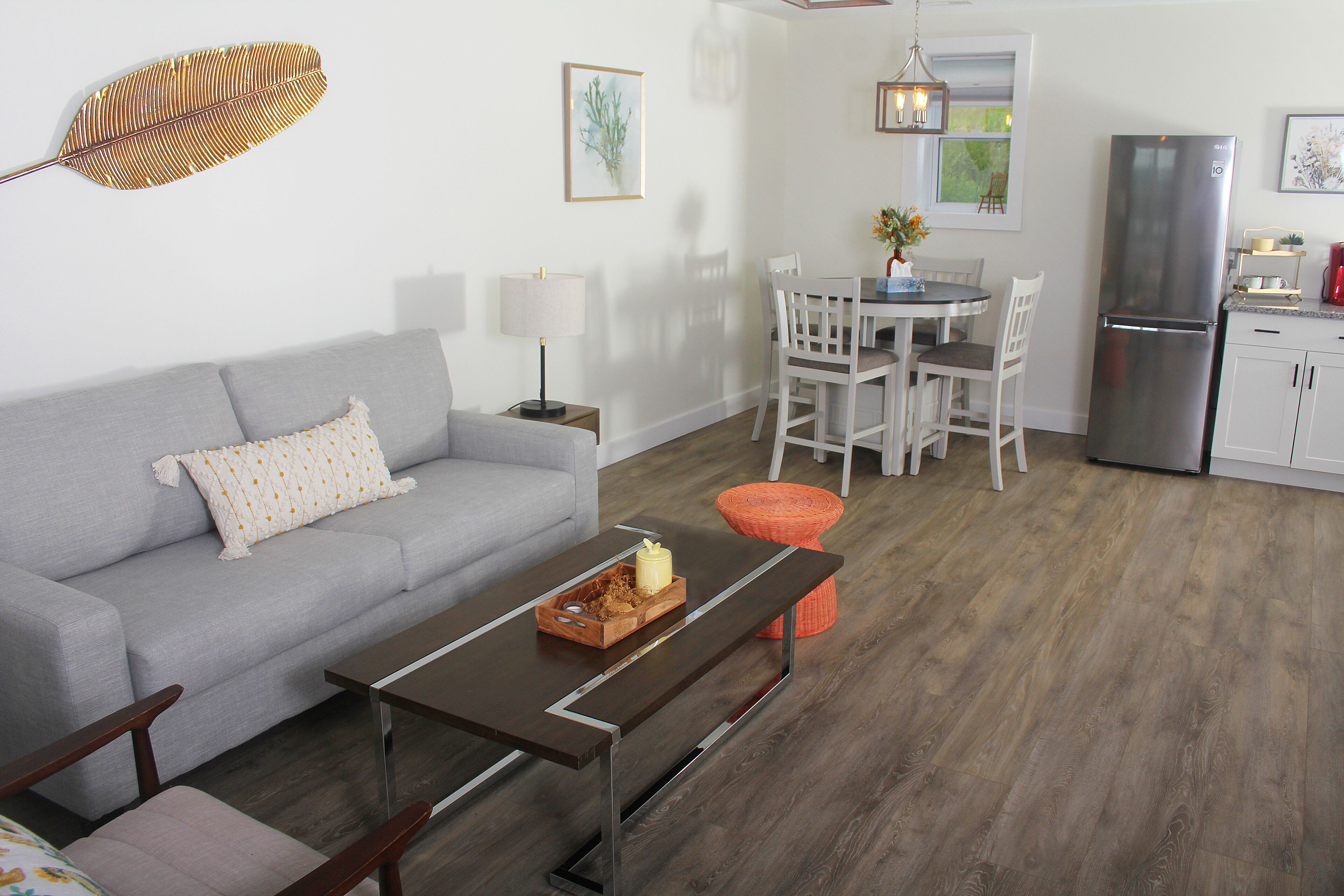 A modern living room with a gray sofa, a wooden coffee table with a candle, and a dining area with a white table and chairs.