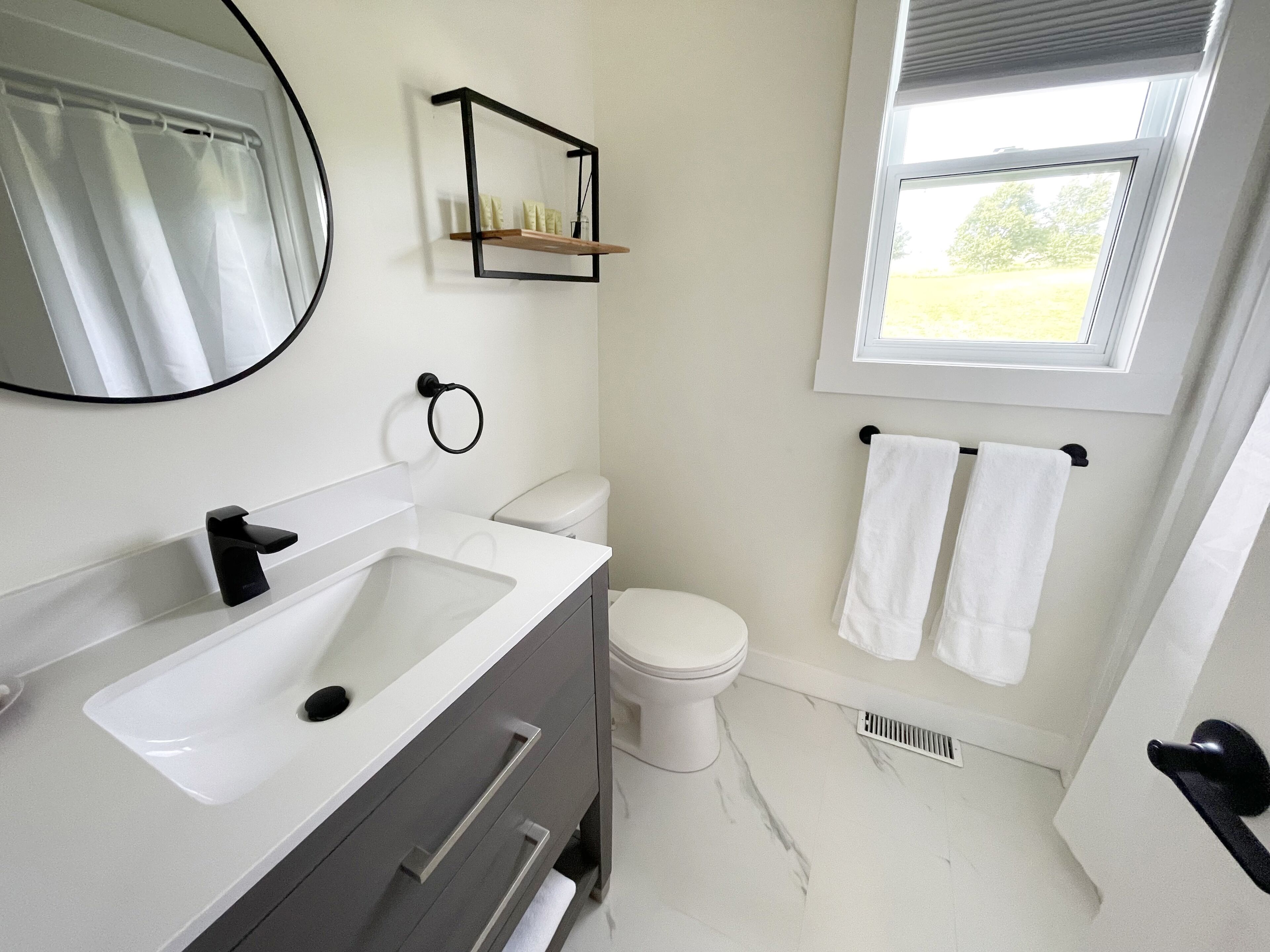 Een moderne badkamer met een wit wastafelmeubel, wc en een raam met uitzicht op groen.