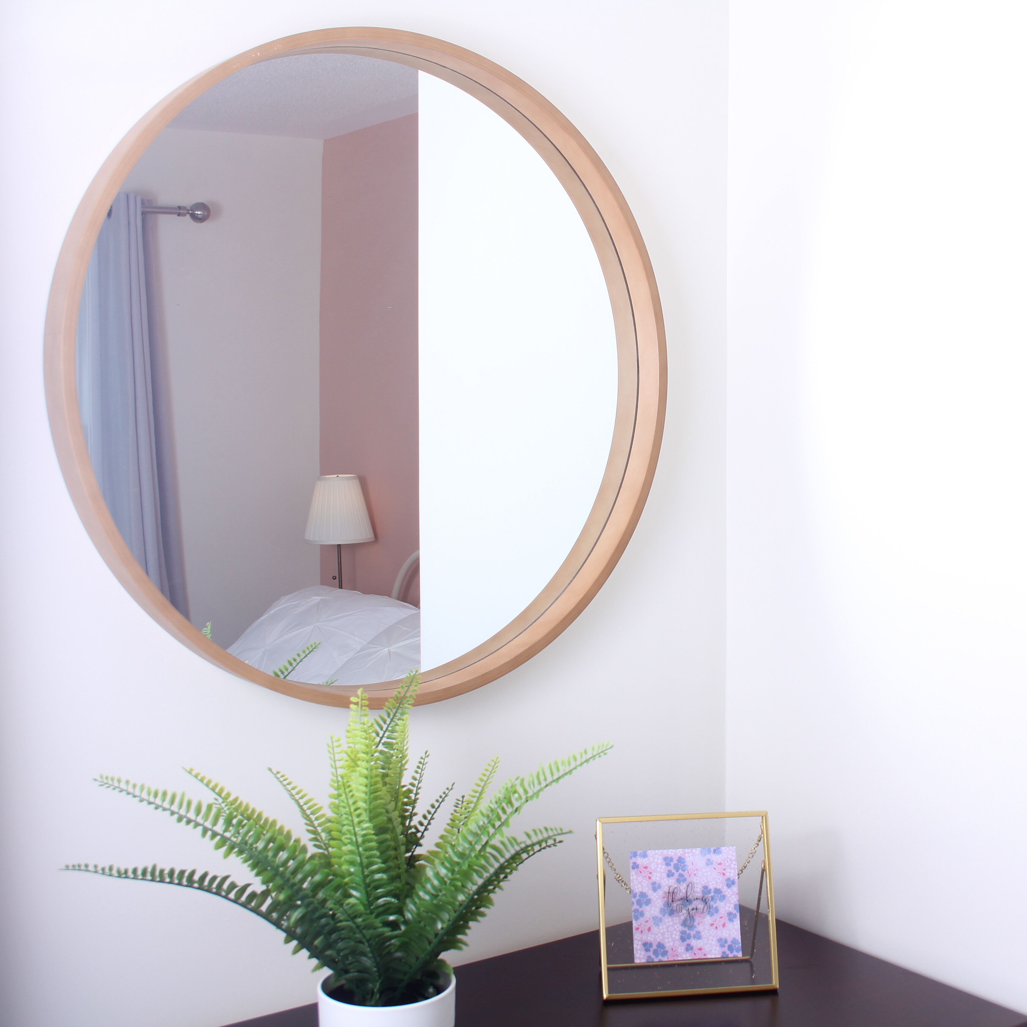 A round mirror on a wall, a potted fern, and a small picture frame with a card.