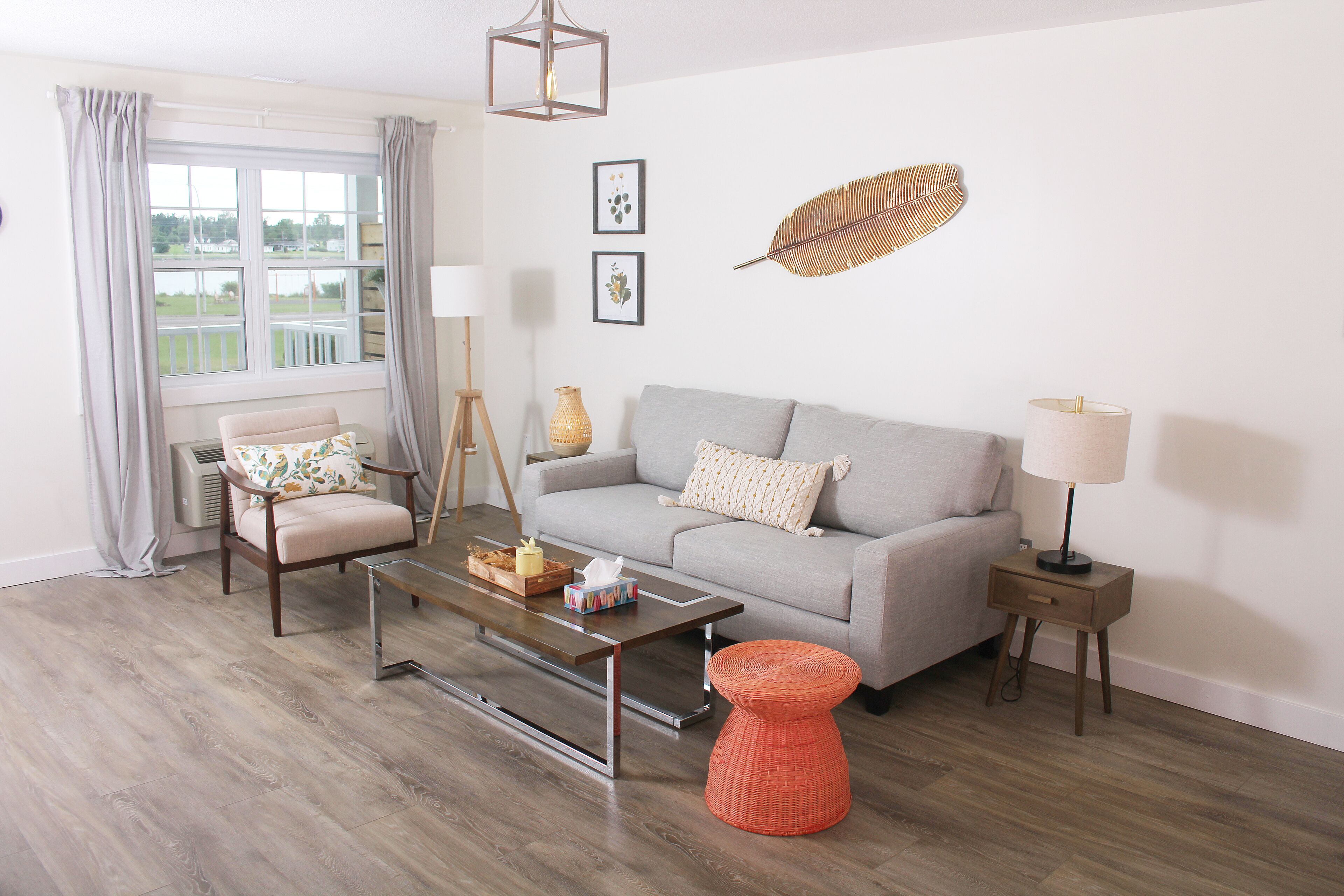 A living room with a grey sofa, a wooden coffee table, a wicker ottoman, and a side table with a lamp.