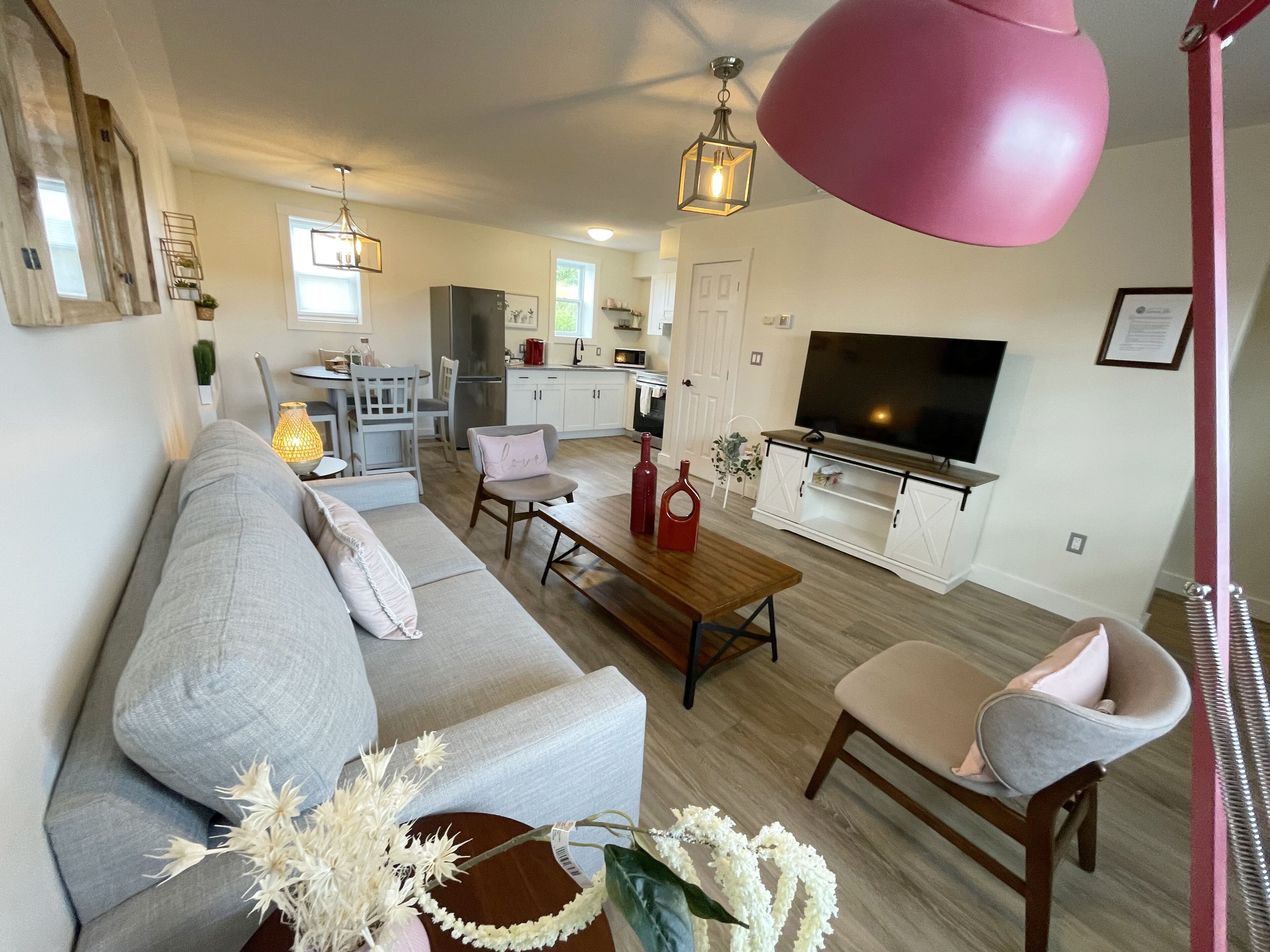 Un salon moderne avec un canapé gris, une table basse en bois et une suspension rose.