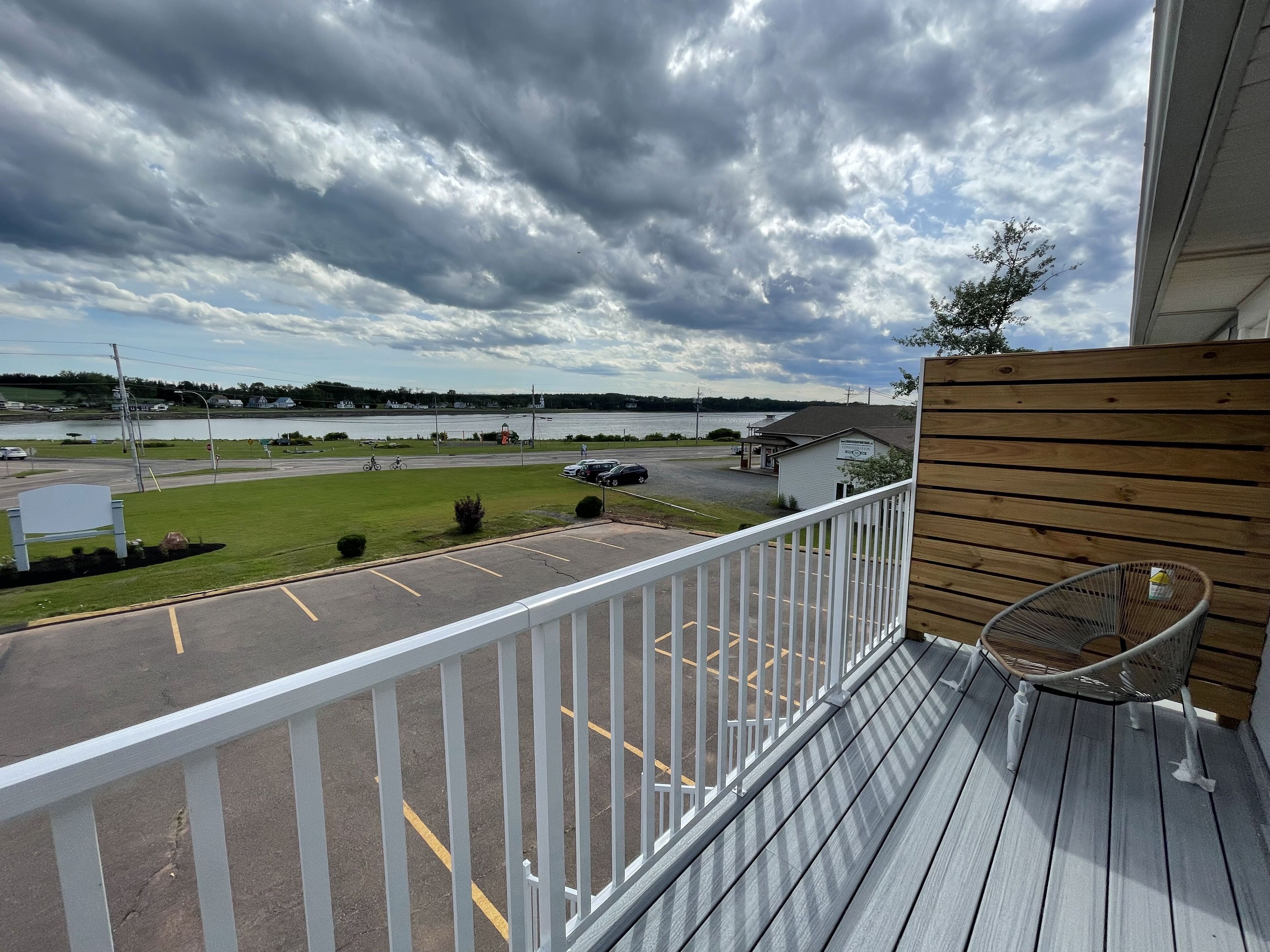 A balcony with a view of a parking lot, a grassy area, and a body of water in the distance.