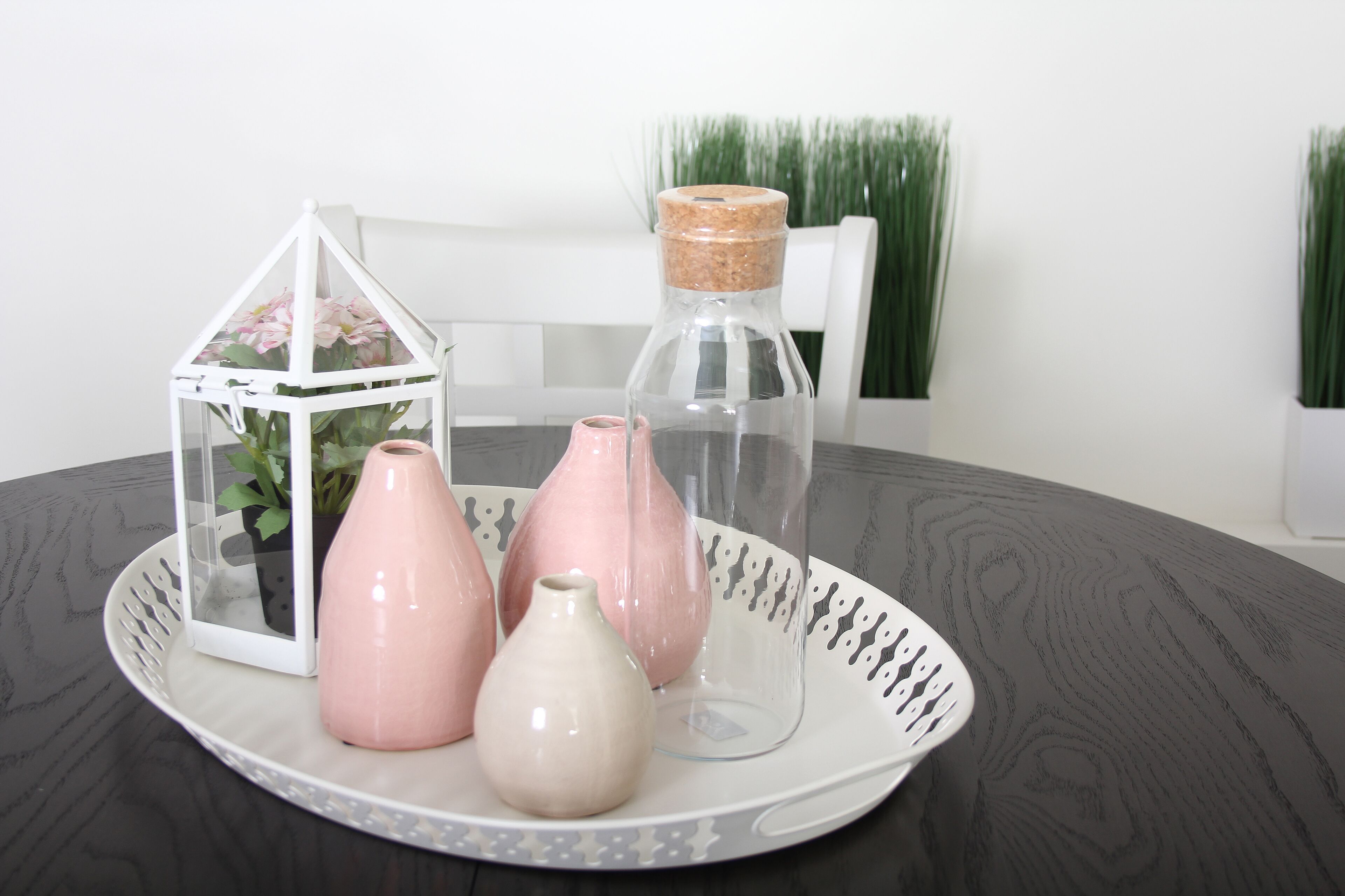 A round table with a white tray holding three vases and a clear glass bottle with a cork stopper.