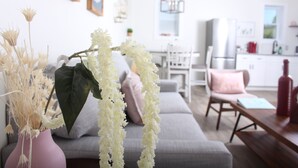 Un salon moderne avec un canapé gris, un vase rose contenant des fleurs séchées et une table basse en bois.