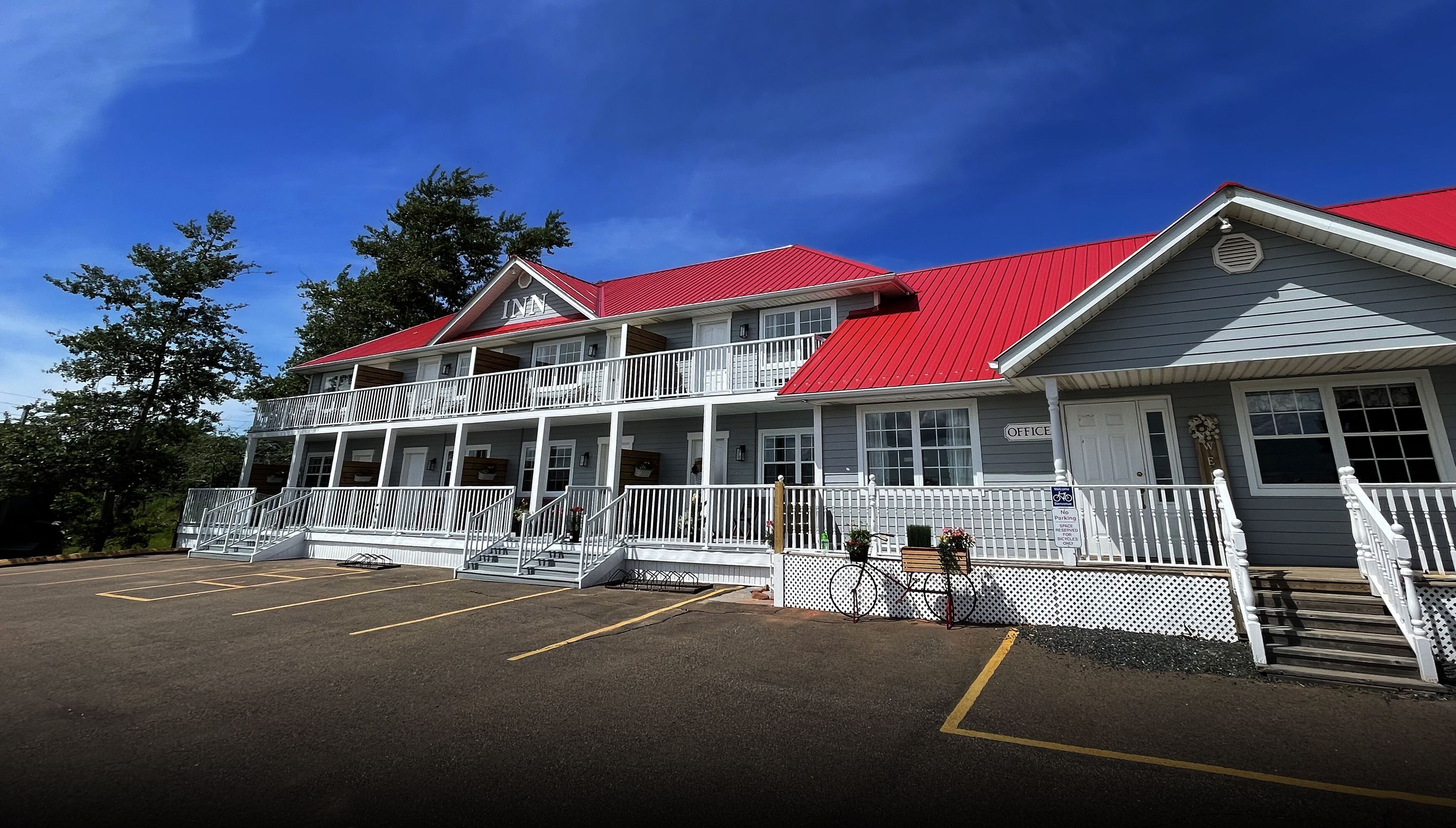 A two-story building with a red roof and white exterior, featuring a porch and a parking lot.