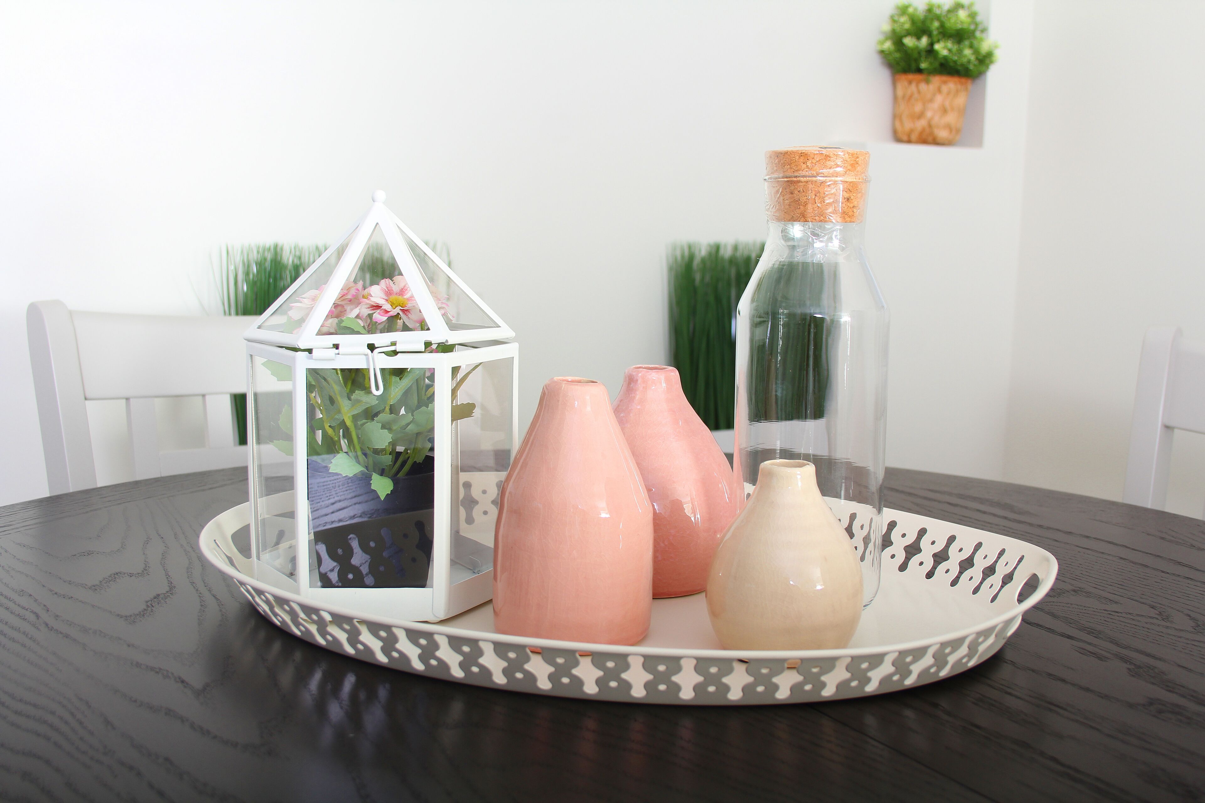 A table with a decorative tray holding three ceramic vases and a glass bottle.