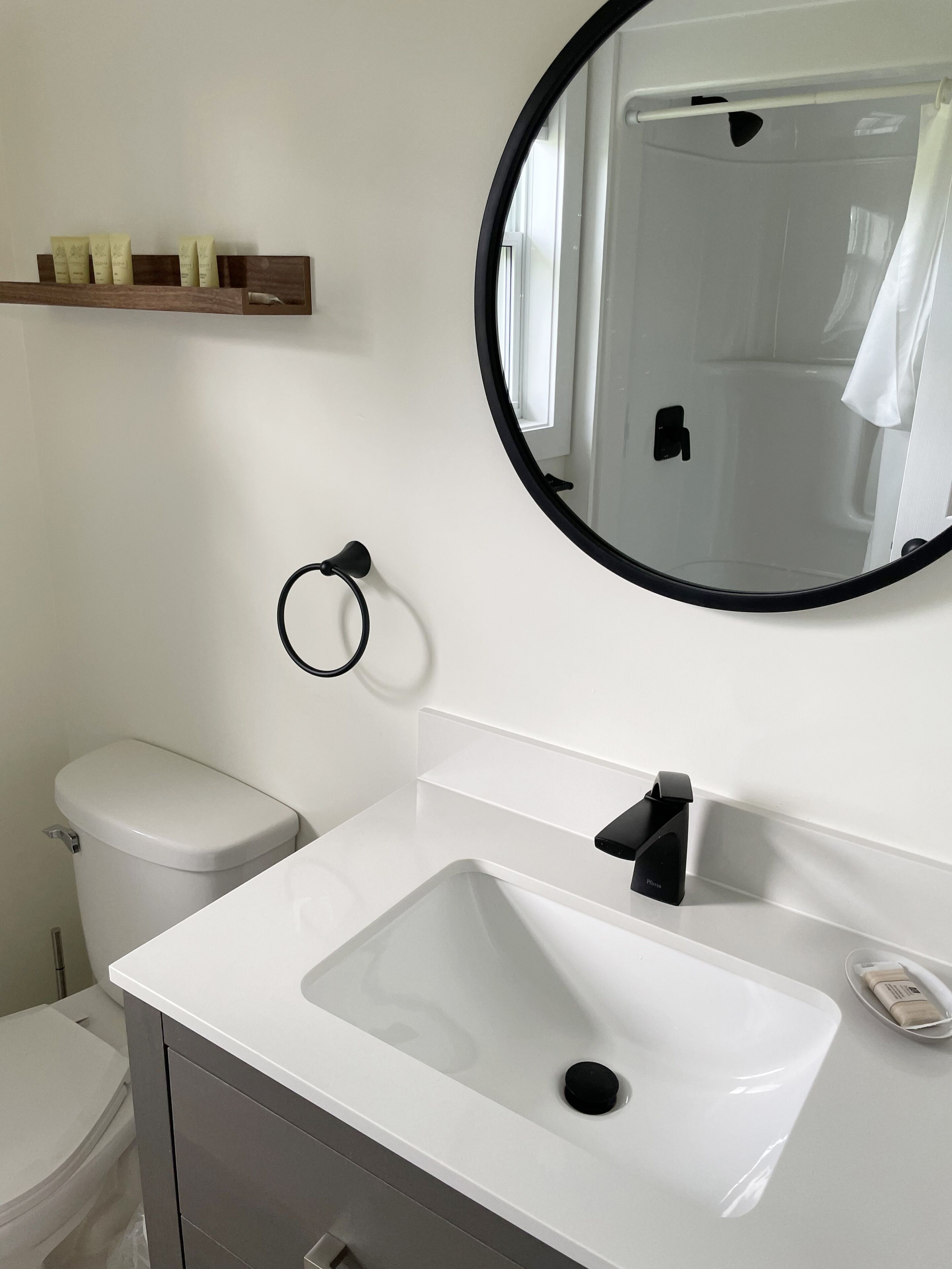 A modern bathroom with a white sink, a round mirror, and a toilet.