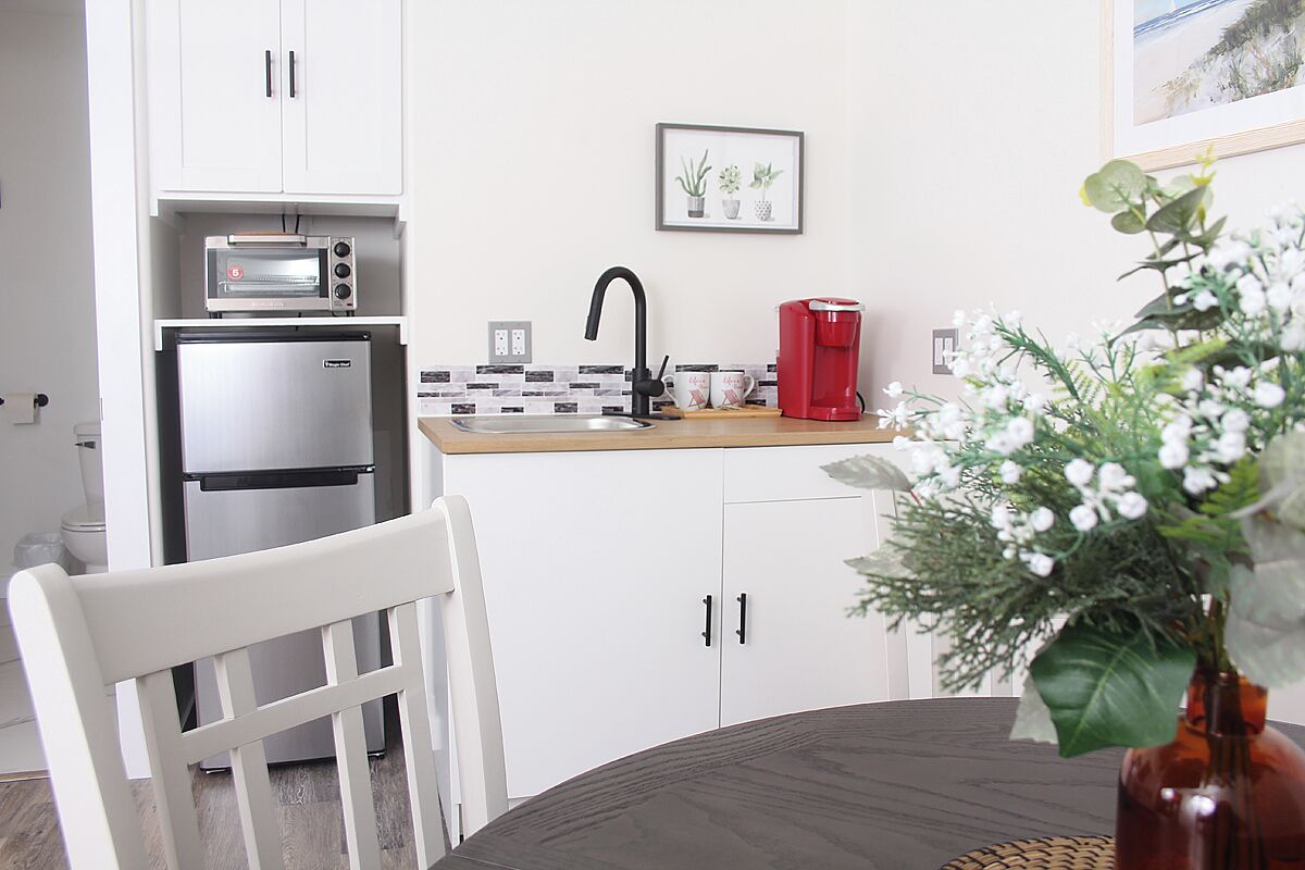 A compact kitchen with white cabinets, a built-in oven, a coffee maker, and a small sink.