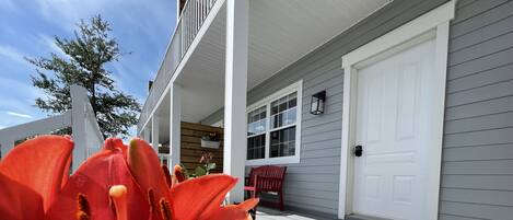 A porch with a red flower in the foreground, a white door, and a bench.