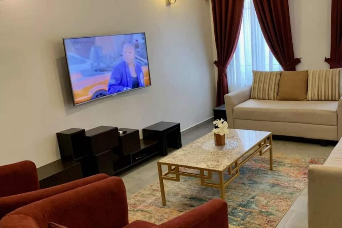 A living room with a TV, sofa, coffee table, and red chairs.