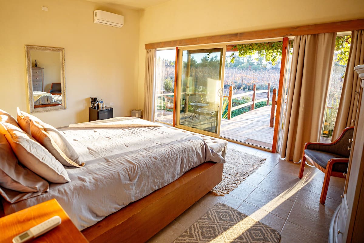 A spacious bedroom with a large bed, a wooden nightstand, a bedside table, a chair, and a sliding glass door leading to a patio.