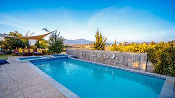 Una piscina al aire libre, sombrillas, sillones reclinables de piscina
