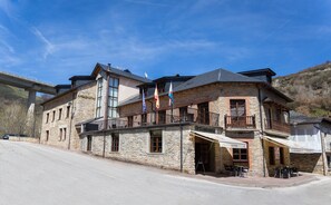 Un edificio de piedra con varios balcones, una cafetería y banderas.