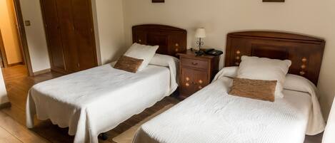 Two single beds with wooden headboards, a nightstand with a lamp, and a wooden wardrobe.