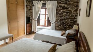 A room with two beds, a wardrobe, a stone wall, and a window with curtains.