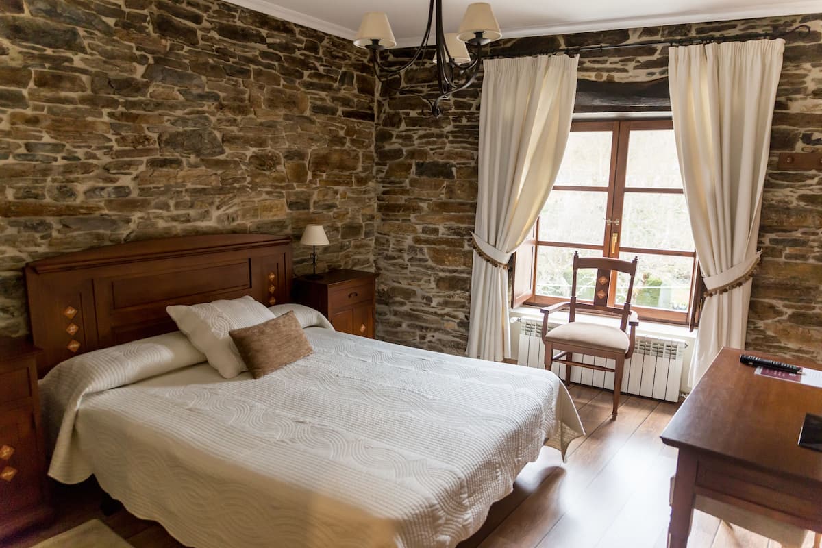 Un dormitorio con pared de piedra, cama de madera, una silla y un escritorio.