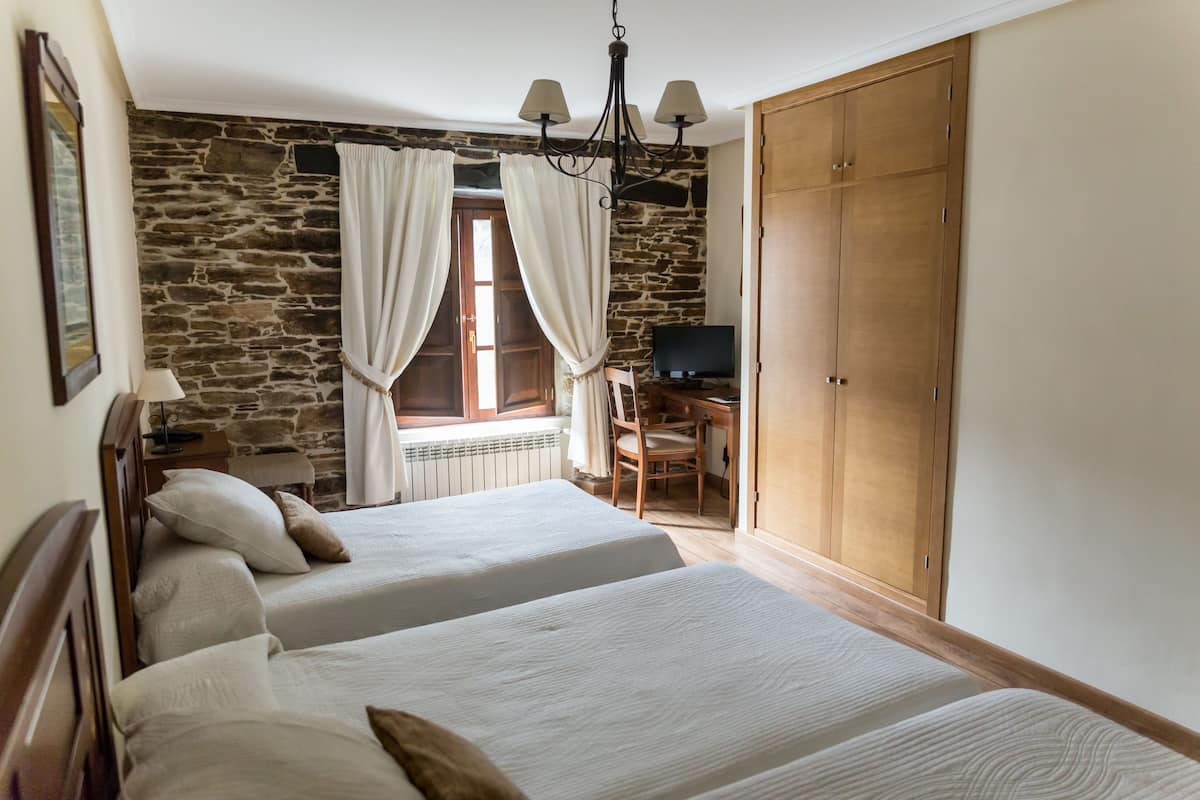 Un dormitorio con dos camas, una pared de piedra, un armario de madera y un televisor.
