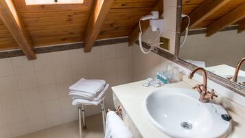 A bathroom with a white sink, copper faucet, and a mirror above it. There is a towel rack with folded towels and a small stool.