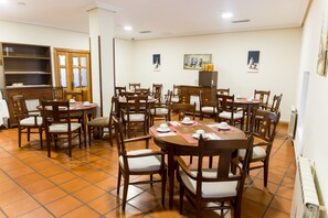 A dining area with multiple wooden tables and chairs, a wooden cabinet, and a tiled floor. - Hotel Ambasmestas (Vega de Valcarce)