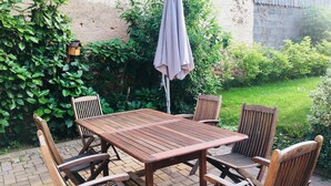 A wooden patio table with six chairs, an umbrella, and lush greenery in the background. - Chambres Au Pied du Haut Koenigsbourg (Kintzheim)